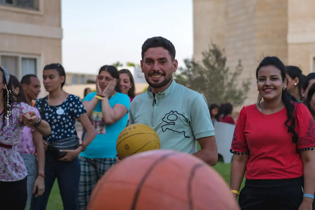 A coach holding a ball mid-game, players watching around him