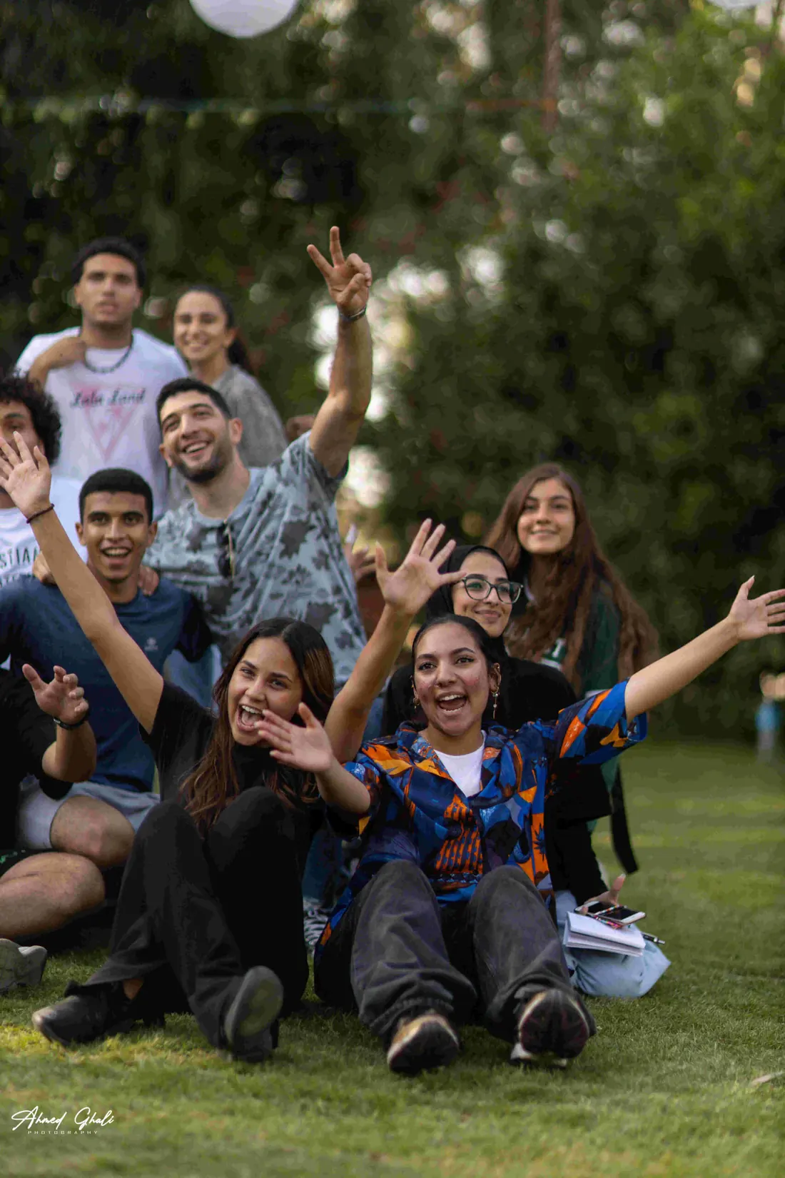 Participants sitting on the grass with arms thrown up, laughing at the camera