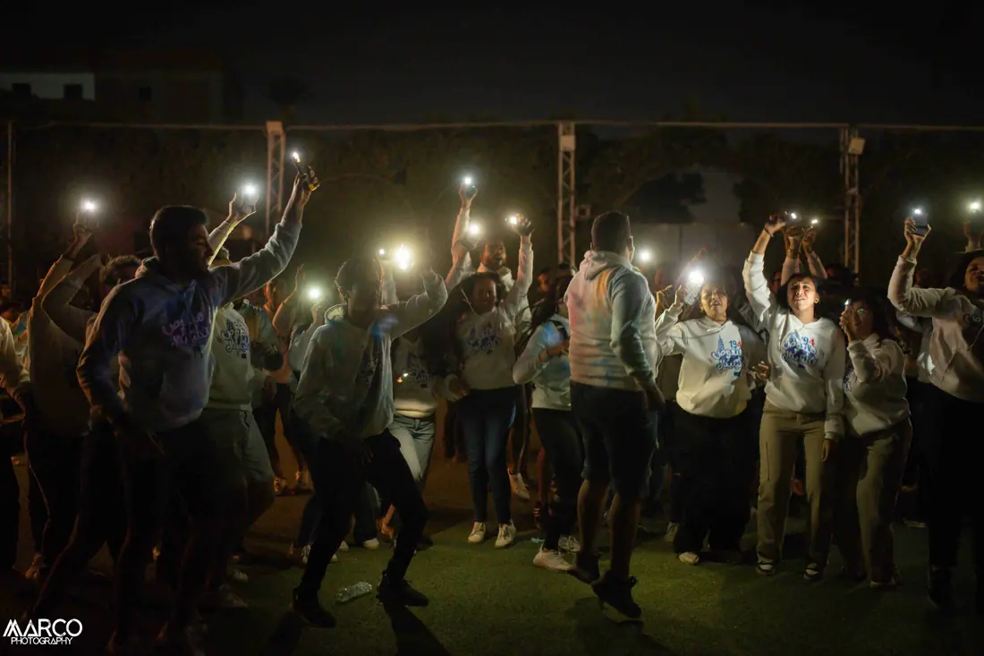 A night crowd dancing with phone torches held in the air