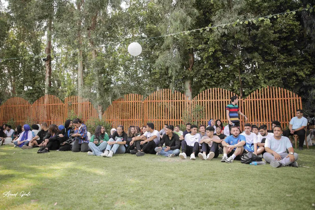 Participants sitting along the grass watching an activity, festoon lights overhead